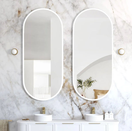 Two oval mirrors on a marble wall above a bathroom vanity.