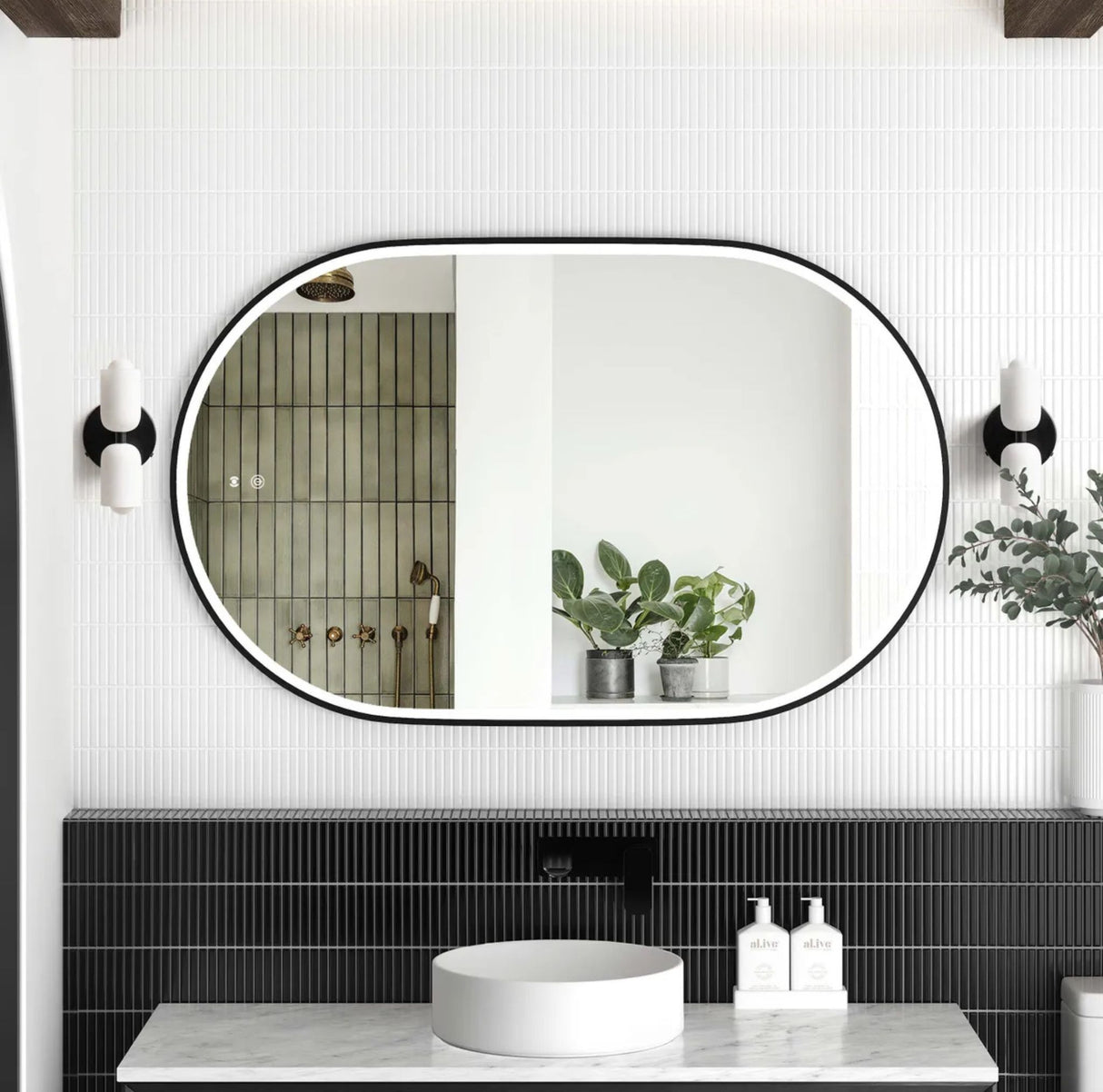 Bathroom with a large oval mirror, black-framed tiles, and white fixtures.