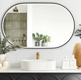 Bathroom with a large oval mirror, white sink, and decorative elements.