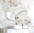Bathroom with marble wall, oval mirror, white sink, and gold fixtures.
