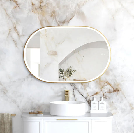 Bathroom with marble wall, oval mirror, white sink, and gold fixtures.