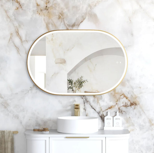 Bathroom with marble wall, oval mirror, white sink, and gold fixtures.
