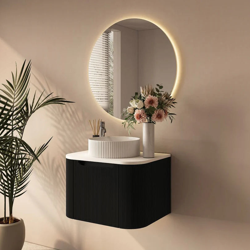 Bathroom vanity with round mirror, sink, and decorative flowers against a beige wall.