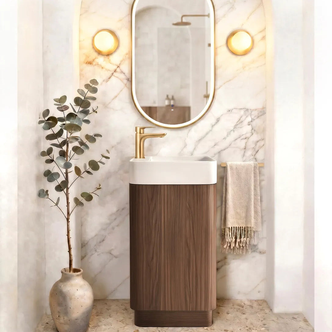 A modern bathroom vanity setup featuring a rectangular white sink with a gold faucet, mounted on a dark wood pedestal. Above it is an oval mirror with a gold frame, set against a marble-patterned wall with built-in round lights.