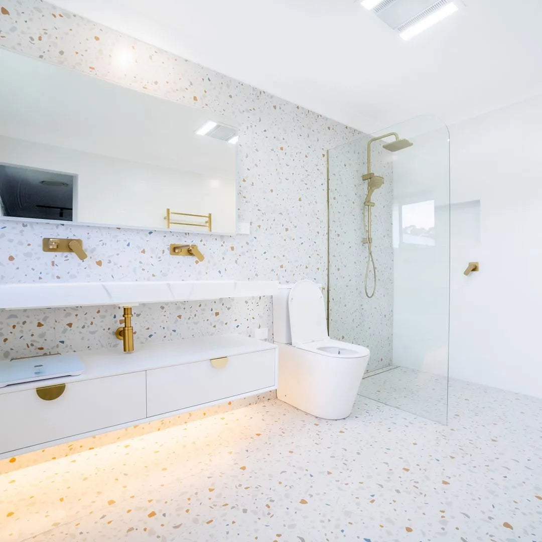 Modern bathroom with white tiles, gold fixtures, and a glass shower enclosure.