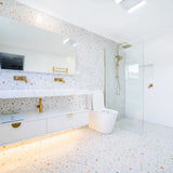 Modern bathroom with white tiles, gold fixtures, and a glass shower enclosure.