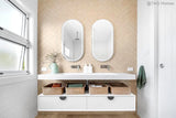 Bathroom vanity with two mirrors, baskets, and toiletries against a beige wall.