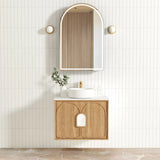 Bathroom vanity with wooden cabinet, round mirror, and decorative elements on a tiled wall.
