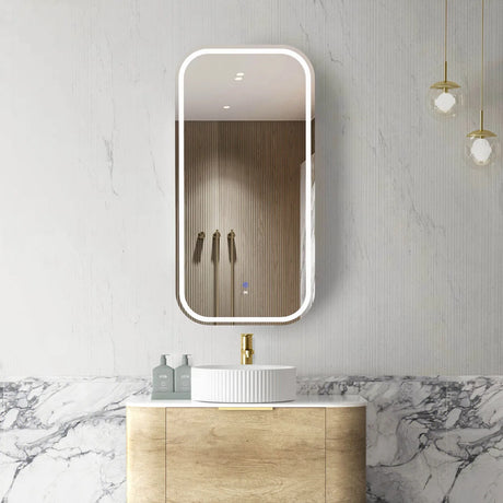 Bathroom with a vanity, sink, and illuminated mirror on a marble wall.