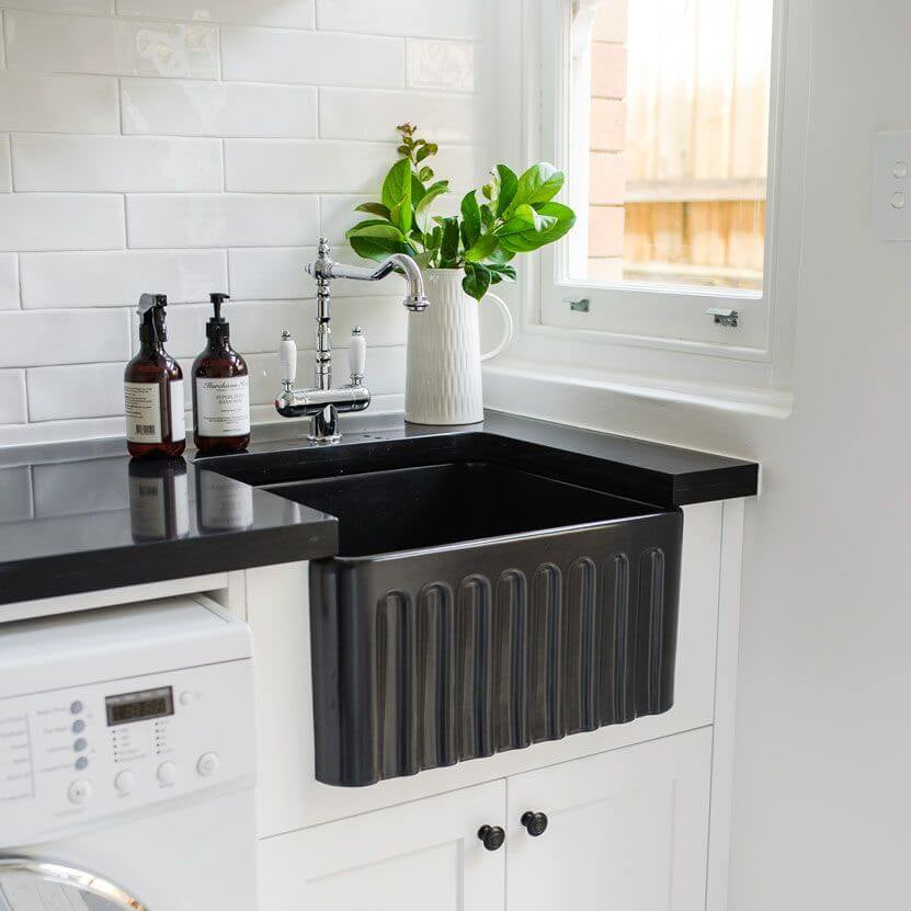 Modern kitchen with black farmhouse sink, white cabinets, and black and white patterned floor.