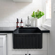 Black kitchen sink in a modern white kitchen with a window and plants.