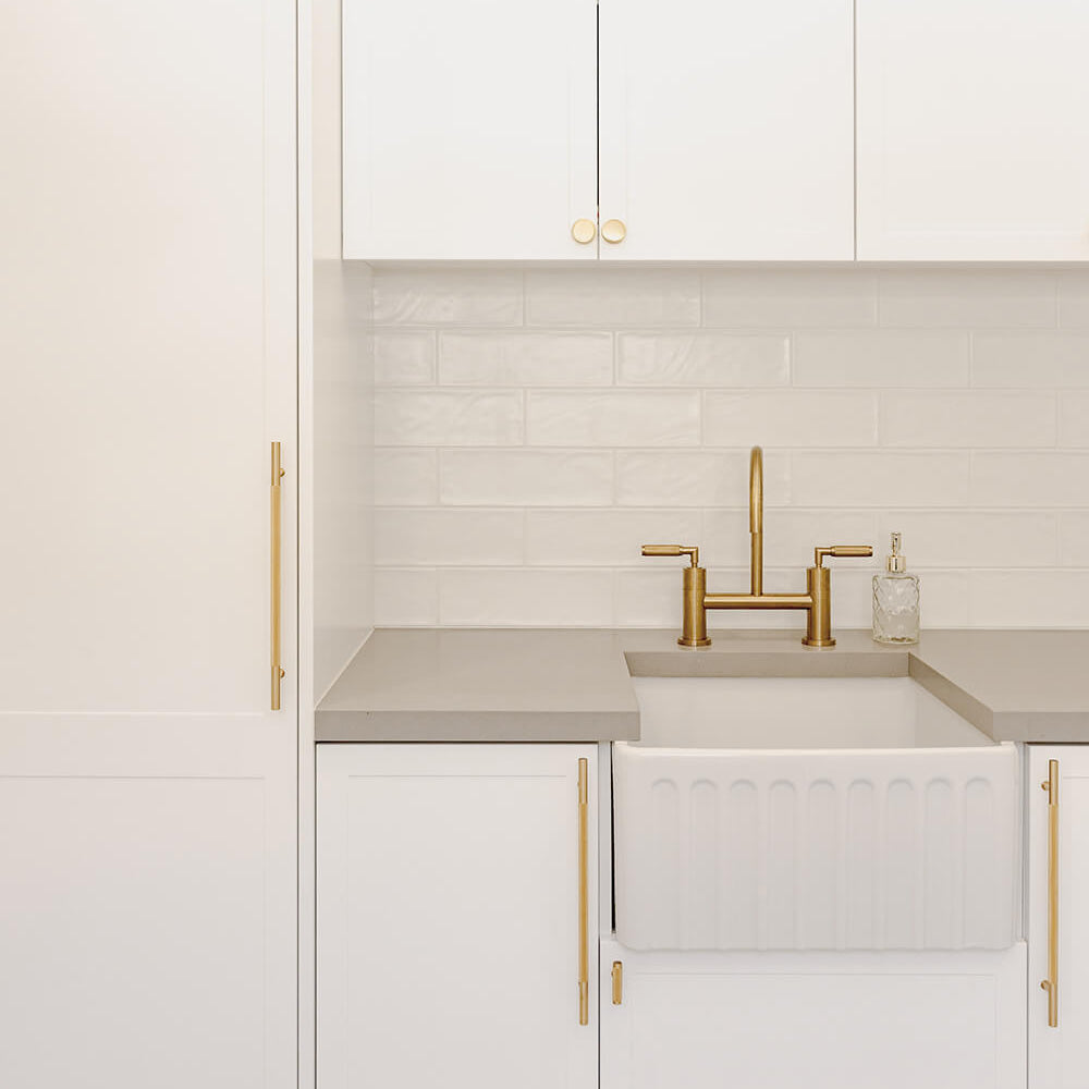 Modern kitchen with white cabinets, gold fixtures, and a tiled backsplash.