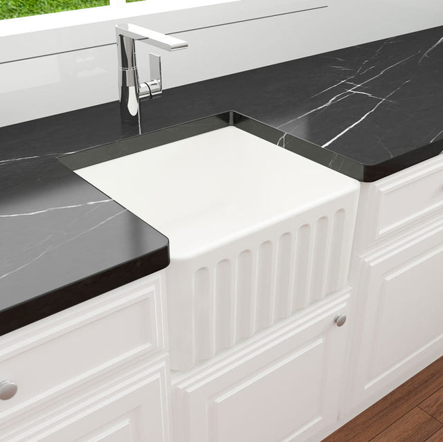 White kitchen sink with black marble countertop and white cabinets.