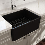 Black farmhouse kitchen sink in a modern kitchen setting with white marble countertop and cabinets.