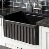 Black farmhouse sink in a kitchen with dark tiled wall and countertop.