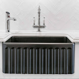 Black kitchen sink with silver faucet against a white tiled wall