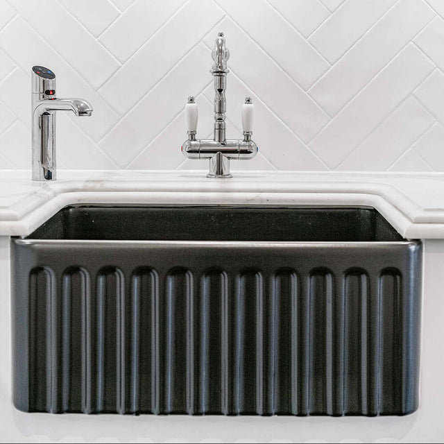 Black kitchen sink with silver faucet against a white tiled wall