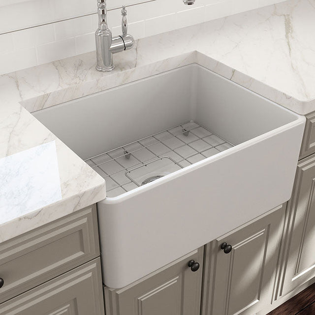 White farmhouse sink in a kitchen setting with marble countertop and cabinets.