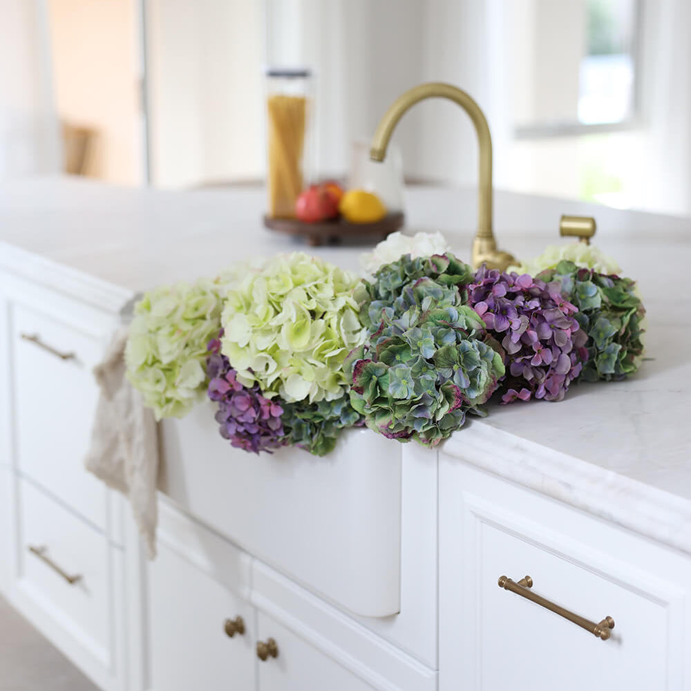 Decorative flowers on a kitchen counter with white cabinets and a sink.