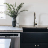 Modern kitchen with black sink, white cabinets, and a vase of greenery on the counter.