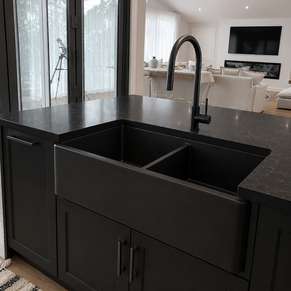A modern farmhouse-style double basin sink in matte black, installed under a matching black countertop with a curved gooseneck faucet, set within dark charcoal kitchen cabinets.