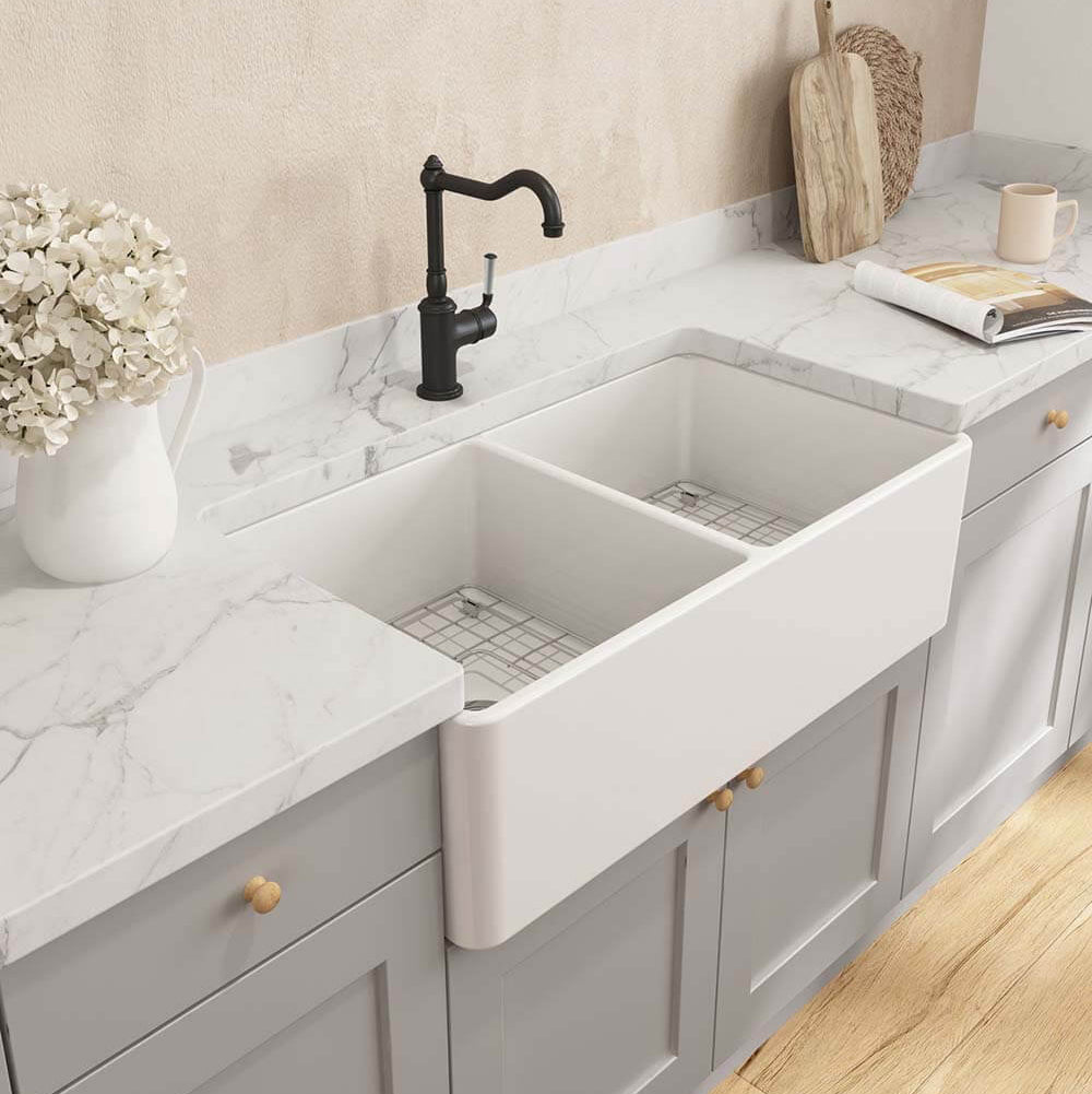 Modern kitchen with a white farmhouse sink, marble countertop, and light gray cabinets.