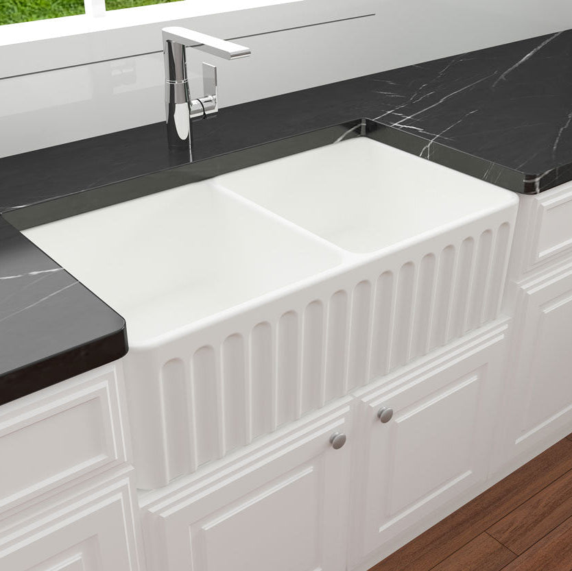 White kitchen sink with black marble countertops and white cabinets.