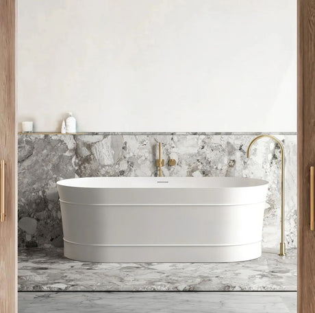 White freestanding bathtub in a bathroom with marble walls and gold fixtures.