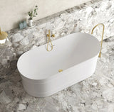 White freestanding bathtub with gold fixtures in a marble bathroom.