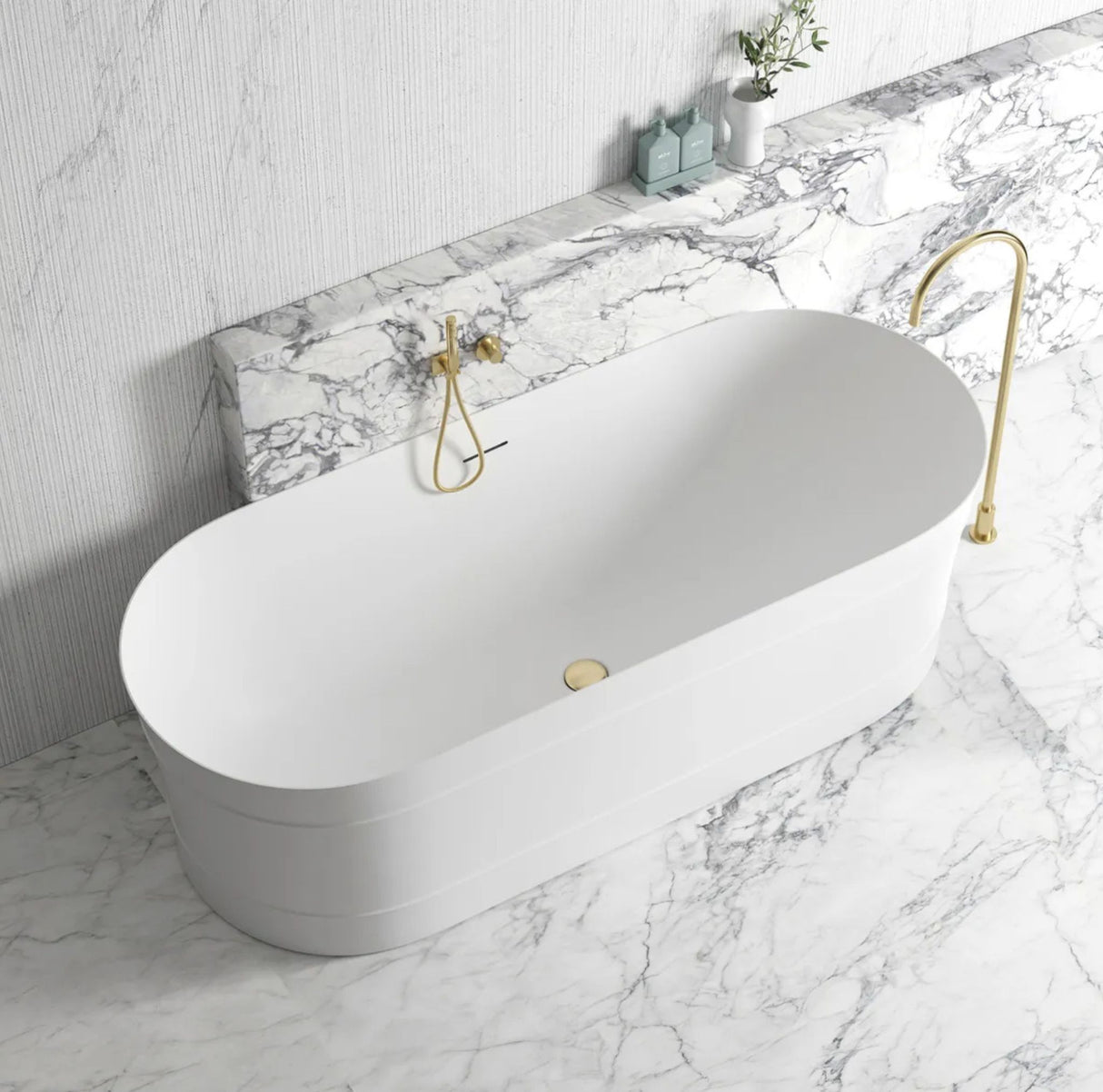 White freestanding bathtub with gold fixtures on a marble floor and wall.