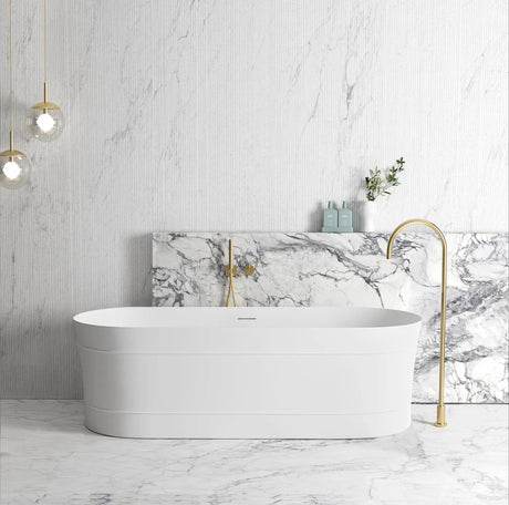 Modern bathroom with a white freestanding bathtub, marble wall, and gold fixtures.