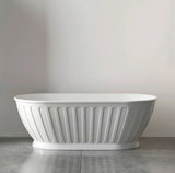 White freestanding bathtub with ribbed design on a gray floor and light gray wall.