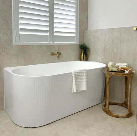 Modern bathroom with a white back to wall bathtub, wooden side table, and decorative elements.