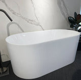 White freestanding bathtub in a bathroom setting with marble wall and plant.