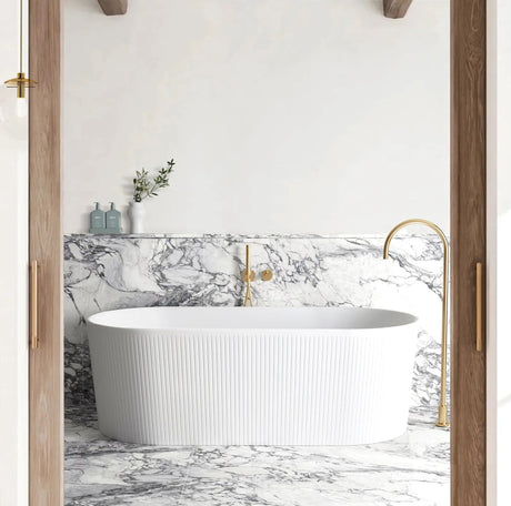 Modern bathroom with a freestanding bathtub, marble wall, and gold fixtures.