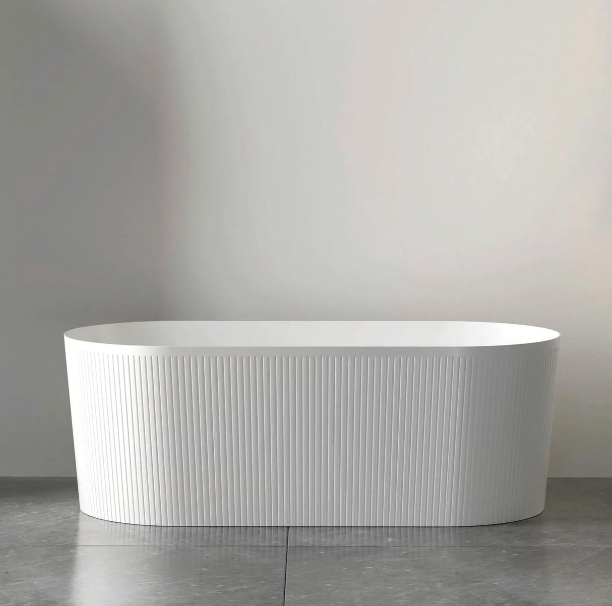 White freestanding bathtub on a gray floor with a neutral gray wall background