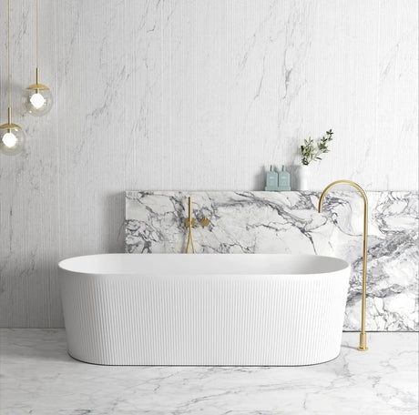 Modern bathroom with a freestanding bathtub, marble wall, and gold fixtures.