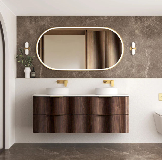 Bathroom vanity with wooden cabinet, white sinks, and oval mirror on a marble wall.
