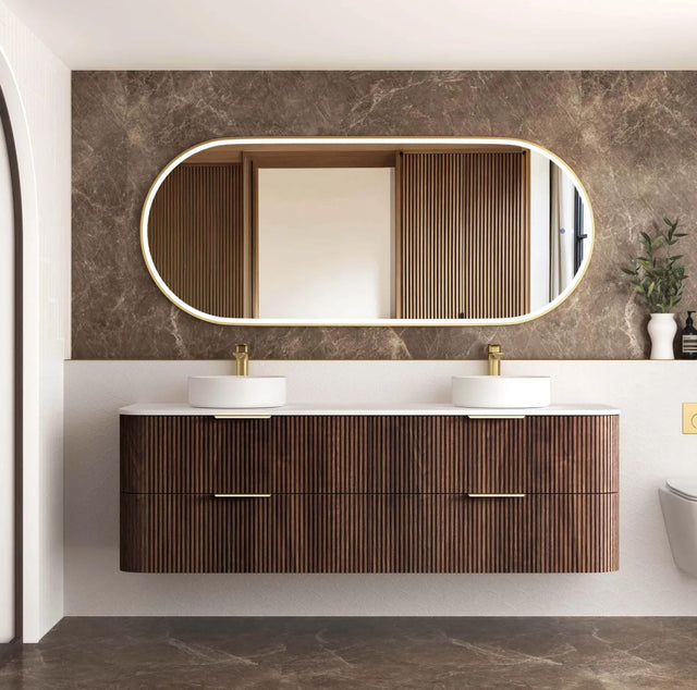 Bathroom vanity with wooden finish, two sinks, and a large mirror on a marble wall.