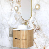 Bathroom vanity with wooden cabinet and white countertop against a marble wall.