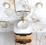 Bathroom vanity with white sink, wooden cabinet, and gold fixtures on marble wall.
