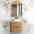 Bathroom vanity with wooden cabinet, round mirror, and towel on marble wall.