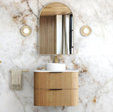 Bathroom vanity with wooden cabinet, round mirror, and towel on marble wall.