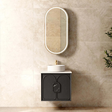 Bathroom setup with a black vanity, white sink, and oval mirror on a beige tiled wall.