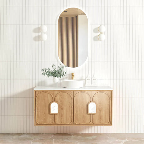 Bathroom vanity with wooden cabinet, round mirror, and decorative plant against a light tiled wall.