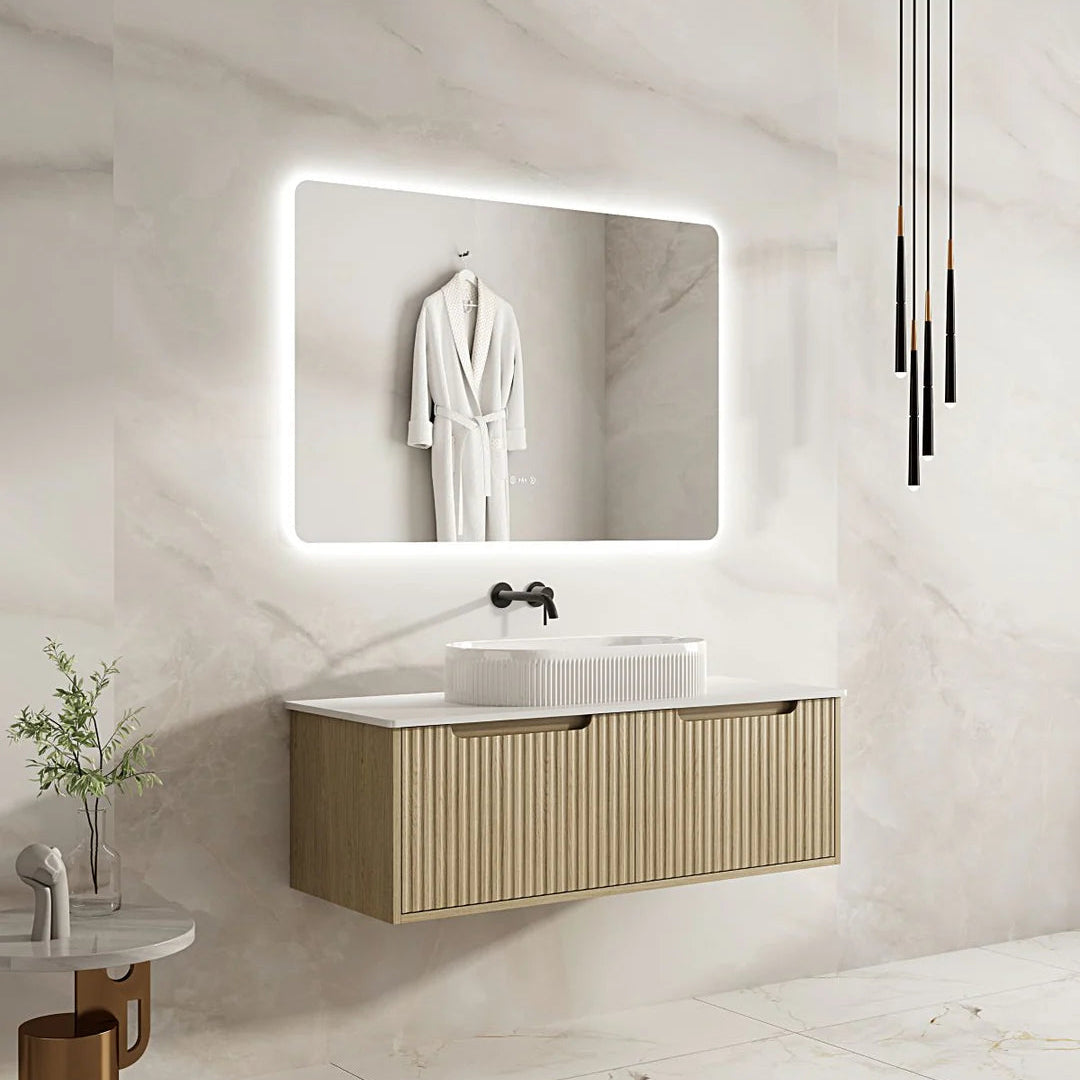 Bathroom vanity with illuminated mirror and white sink against a marble wall.