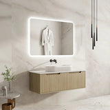 Bathroom vanity with illuminated mirror and white sink against a marble wall.
