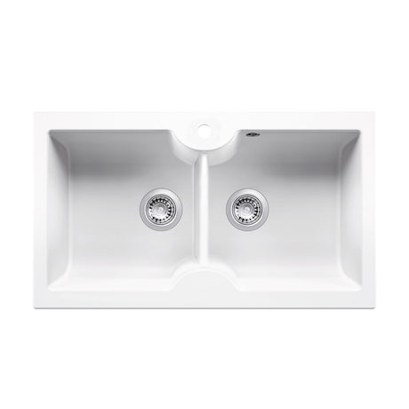 A white double-bowl undermount kitchen sink with two chrome drain strainers and a circular hole in the deck for a faucet, shown against a plain white background.