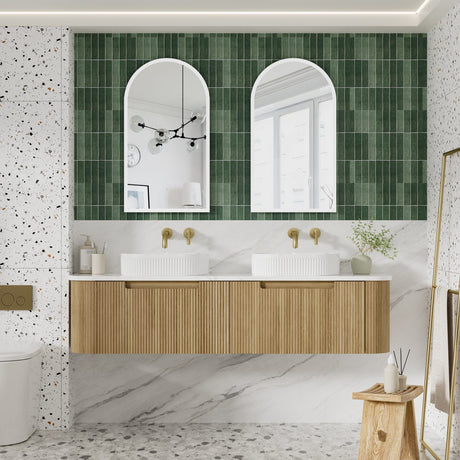 Bathroom with wooden vanity, white sinks, and green tiled wall.