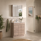 A modern bathroom vanity set featuring a light oak wood cabinet with an integrated white sink, a matching wall-mounted mirror, and a neutral beige tiled wall in a bright, sunlit bathroom.